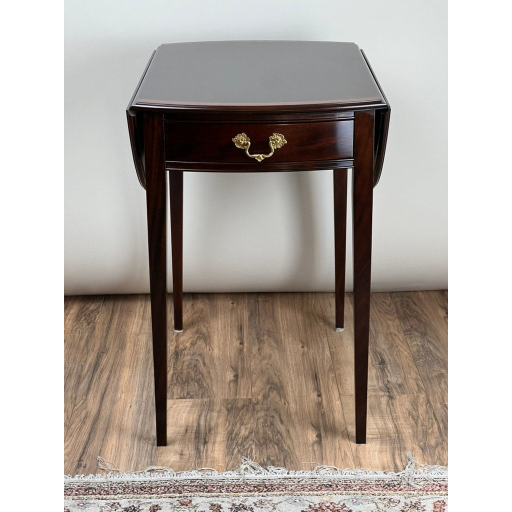 The Vintage Federal Style Edge Banded Mahogany End Table by Stickley features dark wood, a single drawer with a gold handle, and long tapered legs, standing on a wood floor near a patterned rug and plain wall.