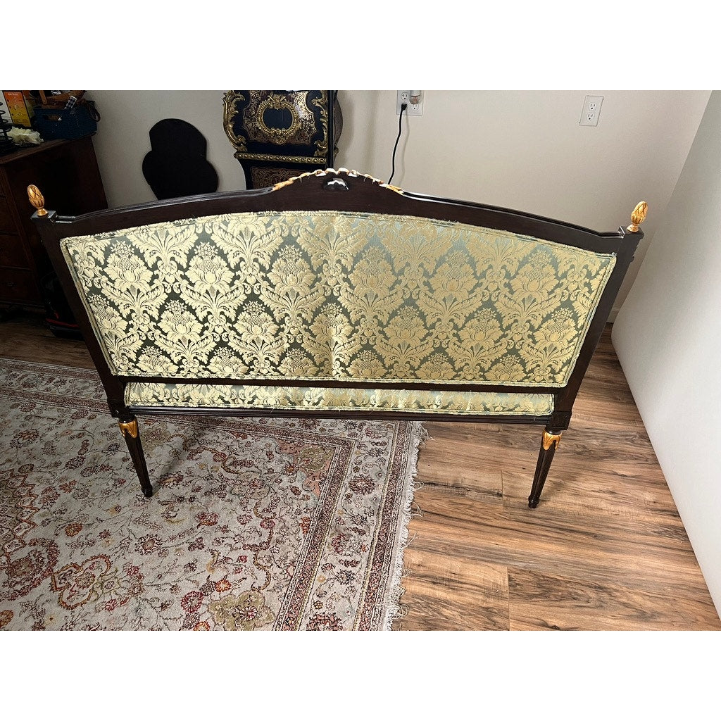 Vintage Louis XVI style settee with green damask upholstery and elegant gold accents, displayed on a hardwood floor near a patterned area rug and white wall. Brand: Unknown.