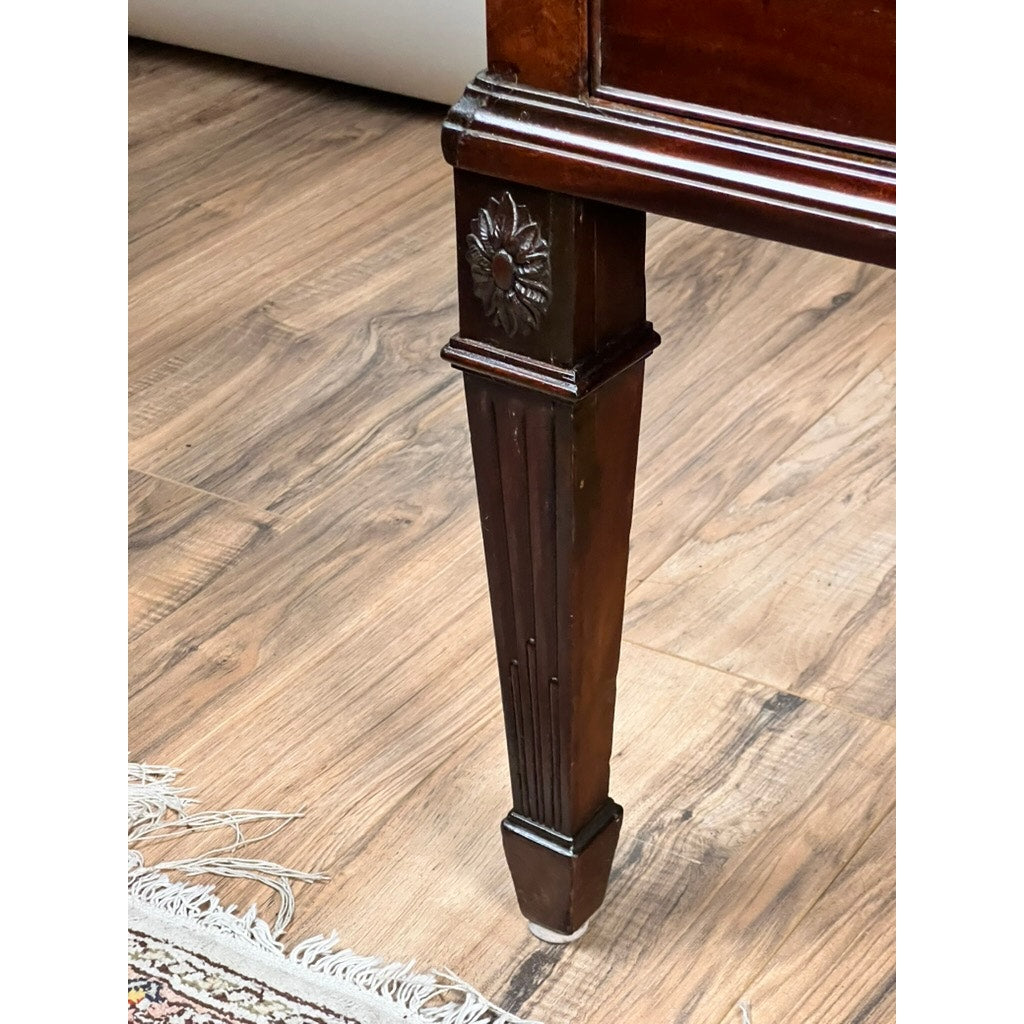 A close-up of a carved leg with a floral motif on an Antique Directoire Style French Cylinder Desk with Slate Top (late 19th century), set on a wood floor beside a patterned rug. Brand: None/Unknown.