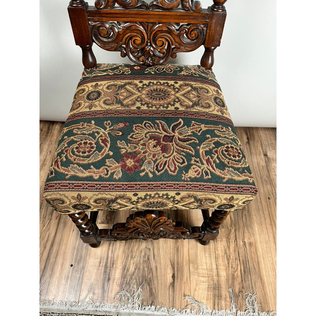 The Antique Carolean Revival Side Chair c. Late 19th Century features an intricately carved back and legs with a green, red, and gold floral geometric upholstered seat, set on a wood floor near a white rug. Brand: Unknown.