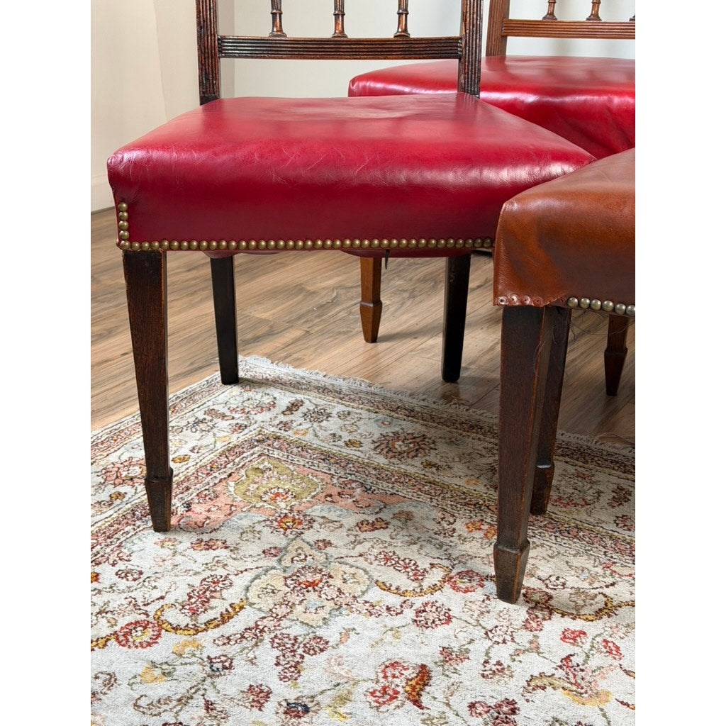 Six English George III mahogany neoclassical dining chairs from Pearl City Antiques, four dating to the 18th century, with red and brown leather seats and nailhead trim, sit on a patterned rug in red and gold tones atop a wood floor.