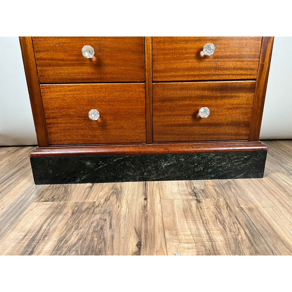 A close-up of the Antique Mahogany Multi-drawer Dental Cabinet by The American Cabinet Co., c. early 20th century, shows four drawers with round glass knobs on a dark base, standing on a wood-patterned floor.