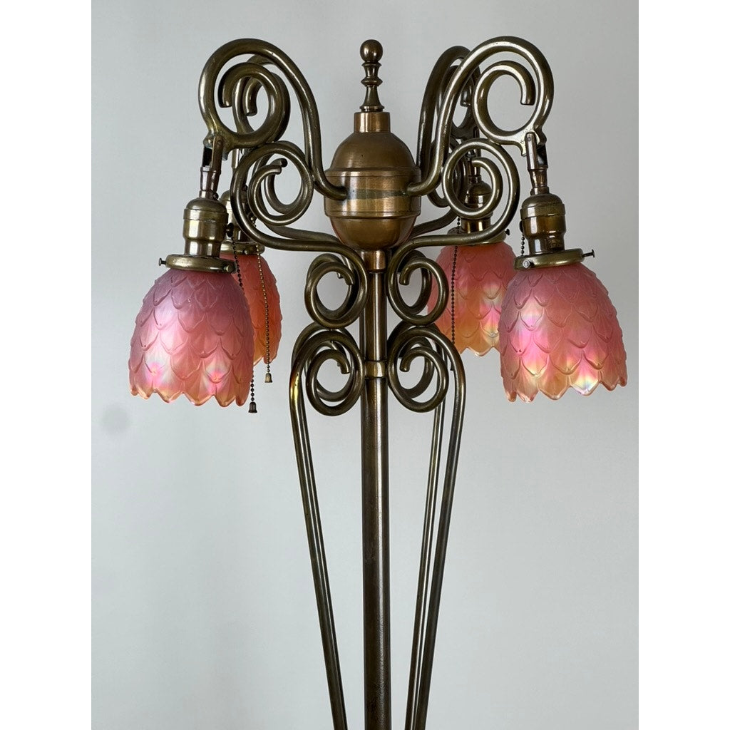 Close-up of an Antique Art Nouveau Brass Floor Lamp attributed to Jules Cayette and Charles Schneider c. 1920, featuring ornate scrollwork, three pink scalloped glass shades, and a pull chain against a plain light background.