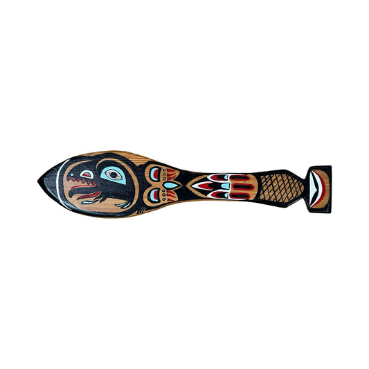 A vintage Inuit carved red cedar paddle from Sitka, Alaska, featuring bold black, red, and teal designs with a stylized face on the head and an illegible signature, displayed on a white background.