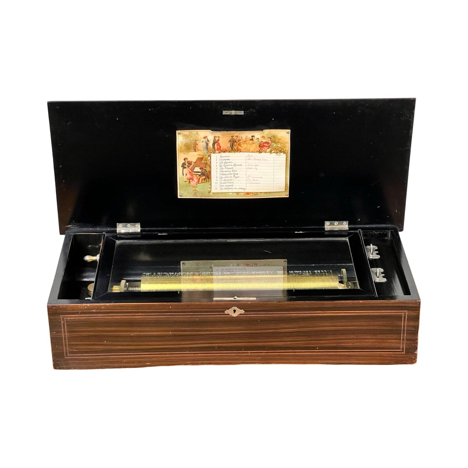 An Antique Swiss 12 Tune Music Box from the late 19th century with its lid open, showing the metal cylinder mechanism and a decorative illustrated label on the inner lid. Brand: None/Unknown.