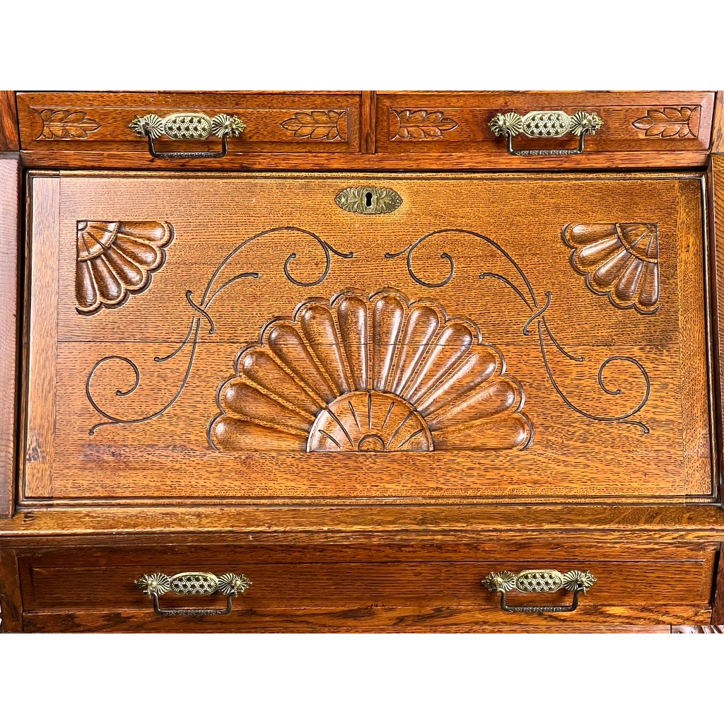 Close-up of an Antique Victorian Oak Ladies Writing Desk c. 1900 with ornate metal handles, intricate floral and scrollwork, a central fan motif, and two shell-like patterns—classic details of a late Victorian era writing desk.