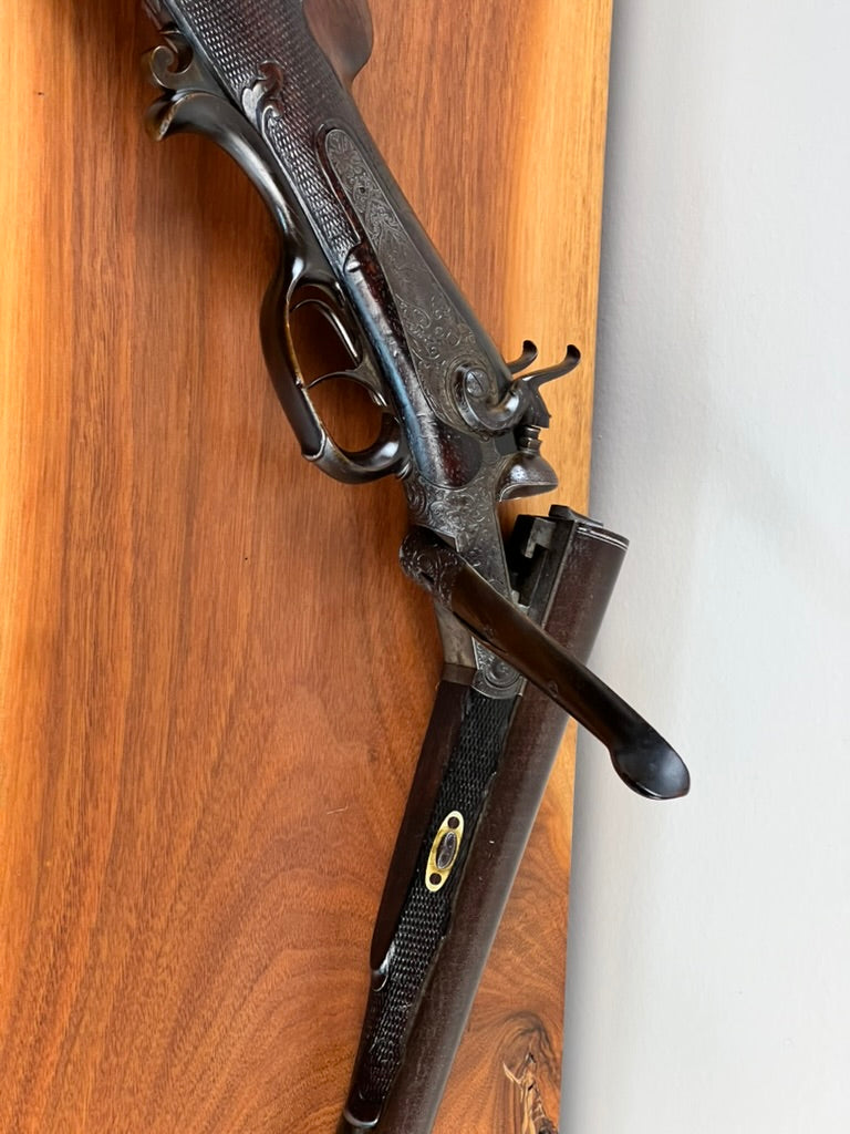 Here is a rewritten sentence using the provided product data: A close-up of the Antique Christoph Funke Suhl German Damascus Double Barrel Hammer Shotgun, c. 1880—offered by Pearl City Antiques—shows its ornately engraved and carved stock, with the shotgun open to showcase beautifully patterned Damascus barrels against a wooden background.