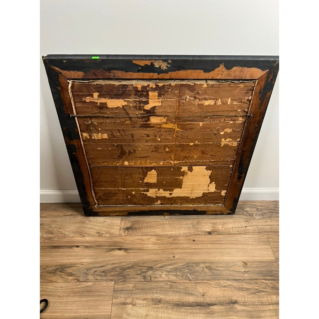 A large antique frame with peeling backing rests against a white wall on wooden flooring. The worn frame likely once held a Japanese Meiji Period Embroidered Painting attributed to Nishimura Sozaemon of Kyoto.