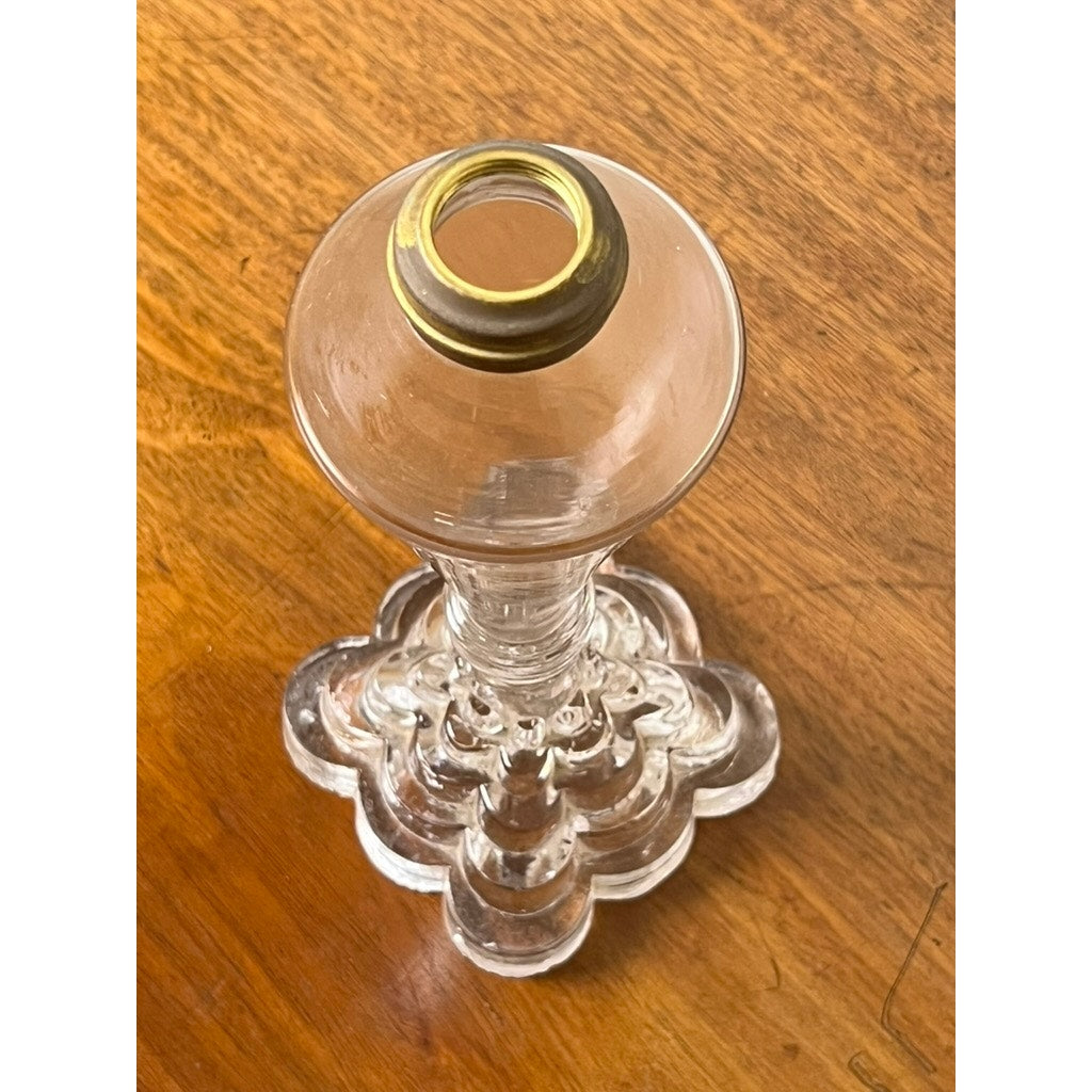 An Attributed Boston & Sandwich Pressed Glass Boudoir Fluid Lamp from circa 1850, featuring clear glass with a gold-rimmed top, rests on a wooden surface and is viewed from above.