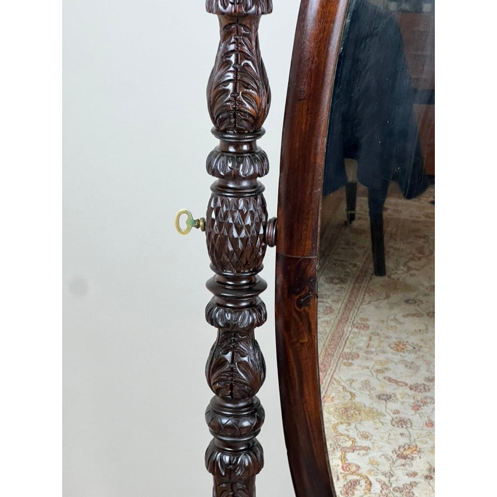 Close-up of an Impressive Antique American Empire Acanthus and Barbola Rose Carved Cheval Mirror c. 1840, featuring a detailed mahogany frame with a key in the side, reflecting a chair and patterned rug—classic 19th-century craftsmanship.