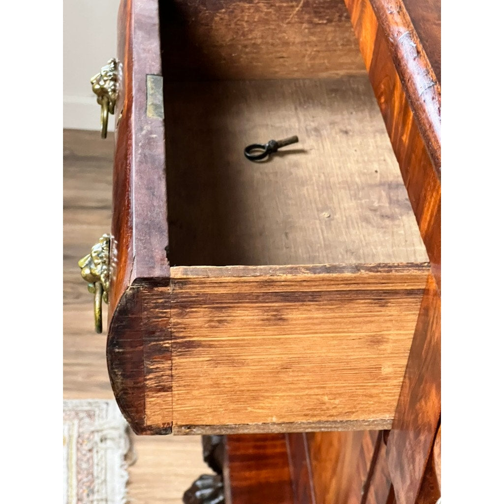 A close-up of an open drawer in an Antique American Empire Mahogany with Rosewood Edge Banding Sideboard, probably Philadelphia c. 1840, reveals a small metal key, ornate brass handles, rich wood grain, and a patterned rug below.