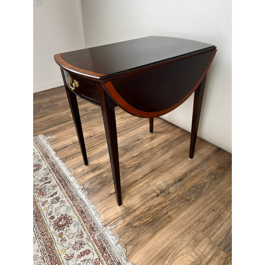 A Vintage Federal Style Edge Banded Mahogany End Table by Stickley sits on a wood floor beside a white wall and patterned rug.