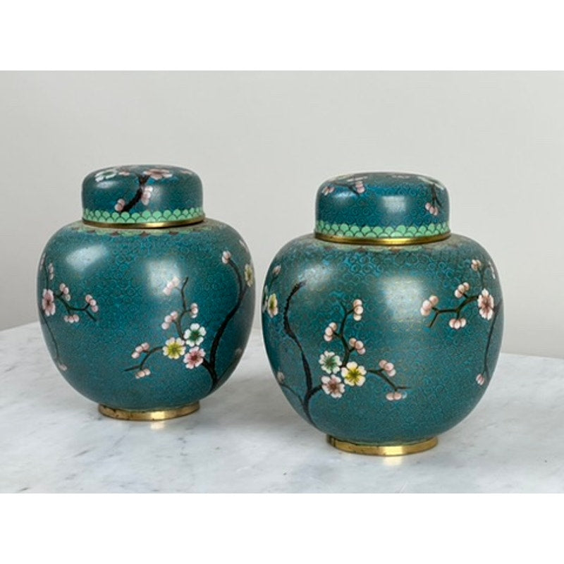 This vintage pair of Chinese cloisonné ginger jars features teal ceramic, floral and branch motifs in pink, white, and green, and matching lids—ideal as decorative accents on a white marble surface against a plain light background.