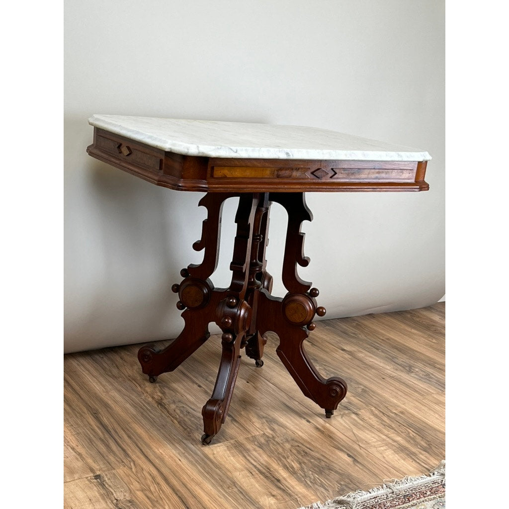 The Antique Eastlake Victorian Walnut Marble Top Stand (c. Late 19th Century) features intricate carvings, curved legs, and a marble top—ideal as an antique plant stand or decorative accent on any wooden floor with a light background.