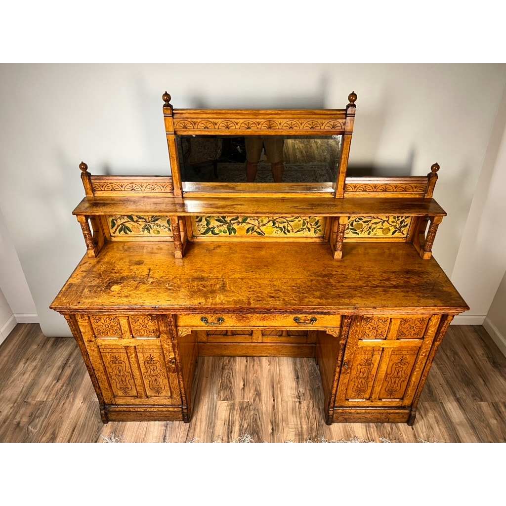 An Antique Victorian Aesthetic Movement oak desk in its original late 19th-century finish stands against a plain wall on a wood floor, featuring elegant period detailing and craftsmanship. Brand: unknown.
