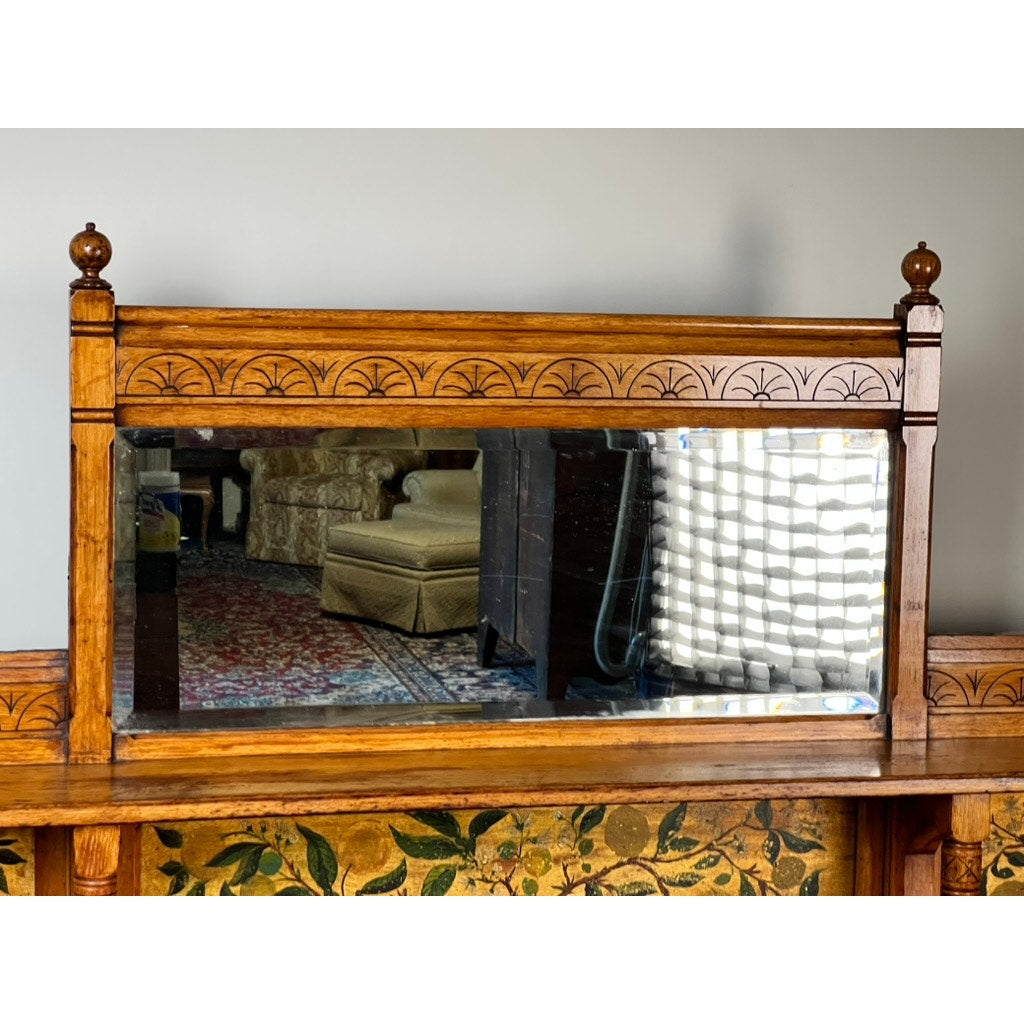 A rectangular mirror with a carved wooden frame and floral motif reflects part of a room, including an Antique Victorian Aesthetic Movement Oak Desk in Original Finish c. Late 19th Century near the window with blinds.