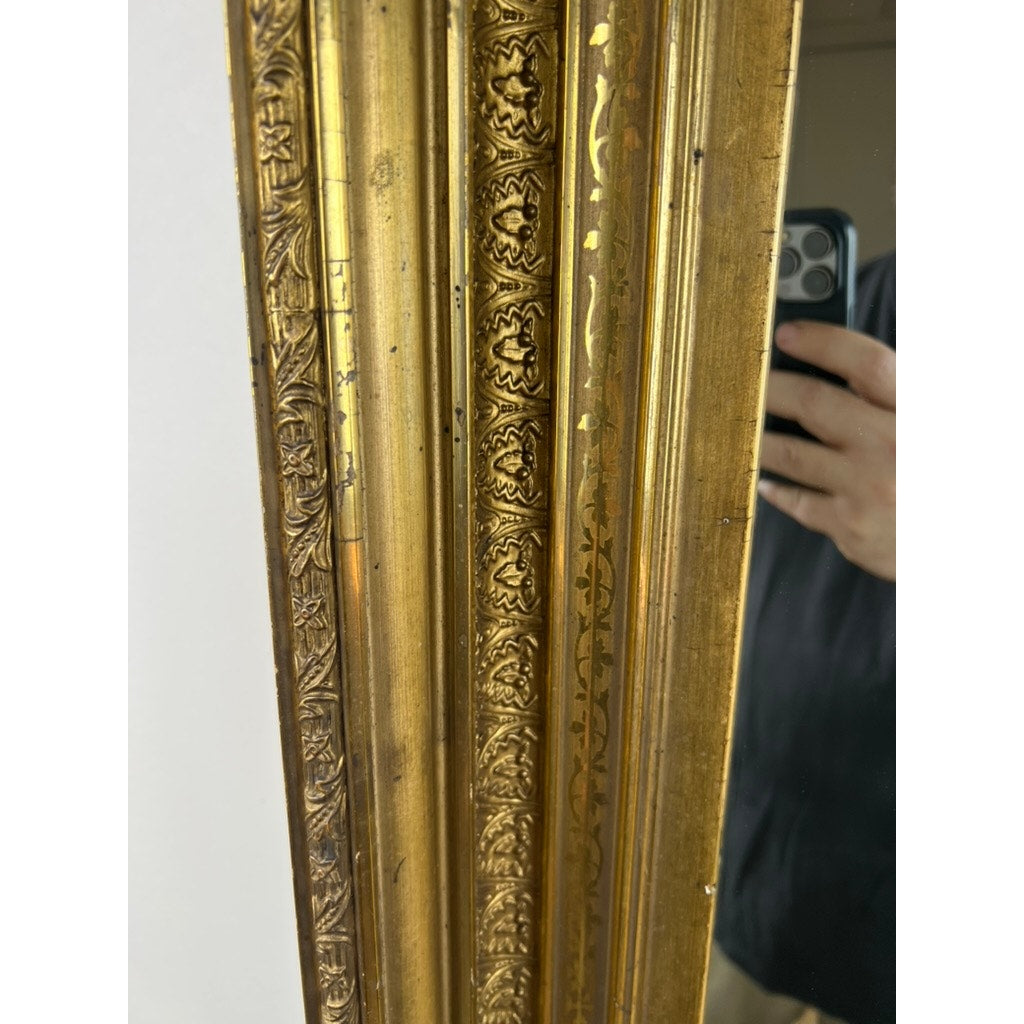A close-up of the Fine Antique 19th Century Gilt Wood Mirror (39 x 34) shows its ornate gold frame with intricate patterns, partially reflecting a person holding a smartphone and serving as a striking antique statement piece. Brand unknown.