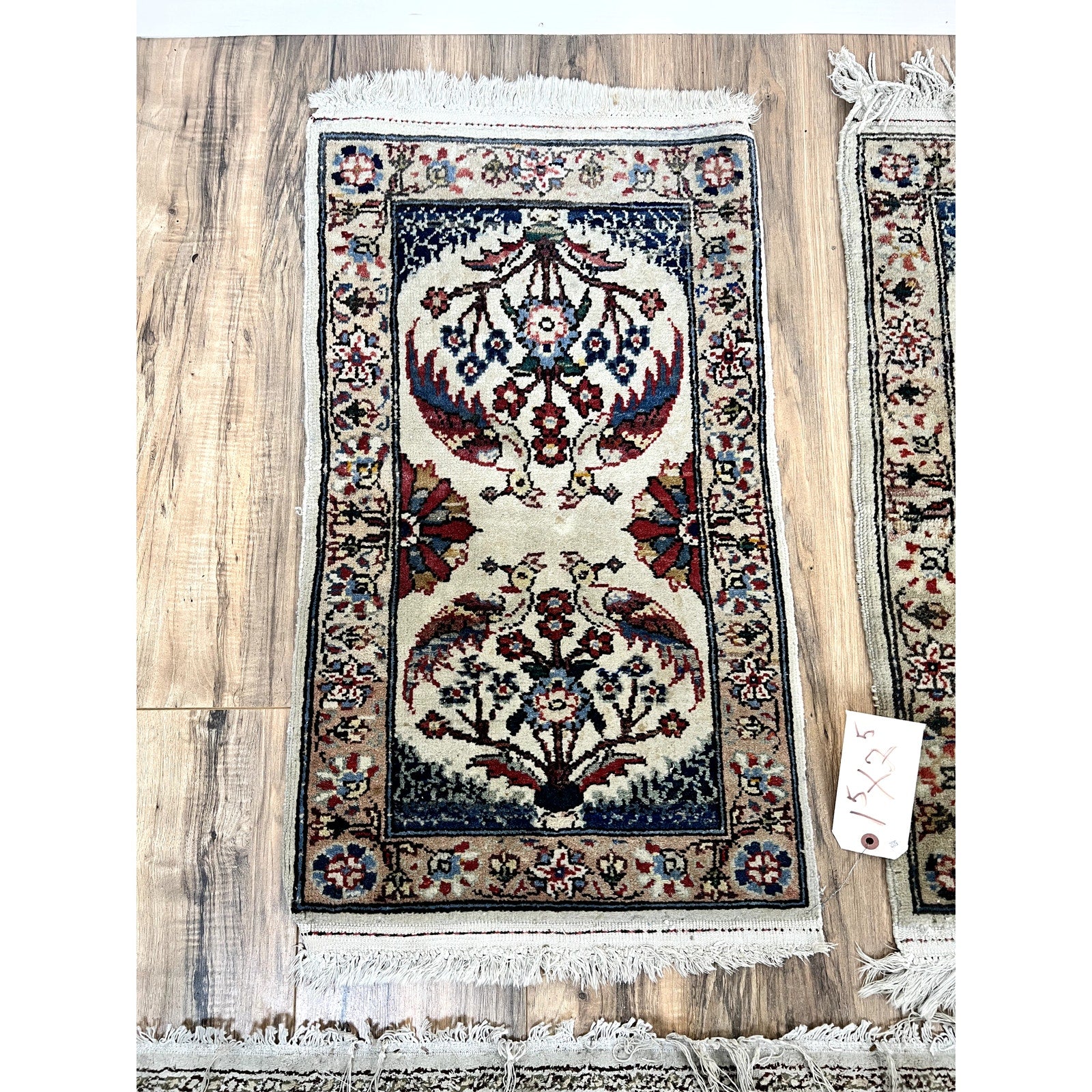 A Vintage Pair of Hand-Knotted Oriental Tree of Life Scatter Rugs (1.5 x 2.5), featuring intricate floral and Tree of Life motifs in red, blue, and beige with fringed edges, rests on a wooden floor; price tag visible.