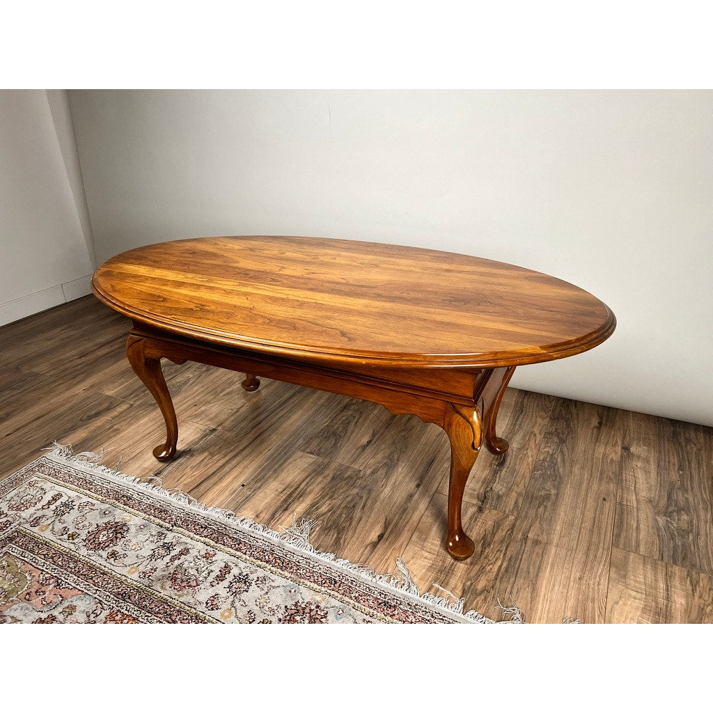 A Vintage Solid Cherry Queen Anne Style Coffee Table attributed to Pennsylvania House stands on a wood floor beside a fringed rug in a bright, minimalist room with white walls.