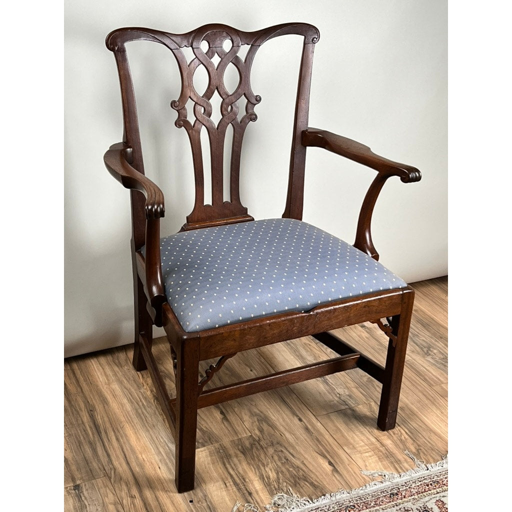 An Antique Chippendale Walnut Open Arm Chair, c. Late 18th Century, with an ornate carved backrest and blue upholstery with white dots, is placed on a wooden floor beside a patterned rug.
