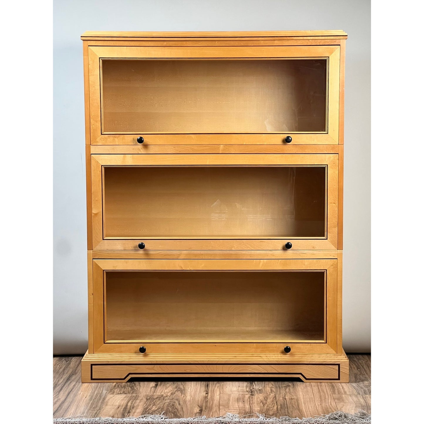 Vintage Bench Made Maple with Wenge Inlay Three Stack Barrister Bookcase featuring glass fronts, a flat top, and three tiers stands on a wooden floor against a plain light-colored wall. Brand: None or Unknown.