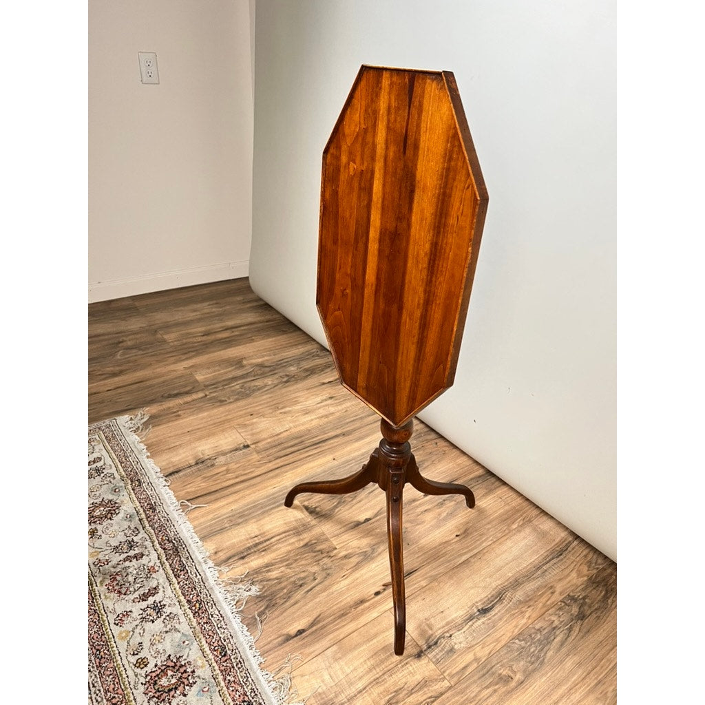 The Stickley Vintage Federal Style Cherry Octagonal Tilt Top Candlestand features a polished surface and three curved legs, shown on a wooden floor near a light wall and patterned rug.