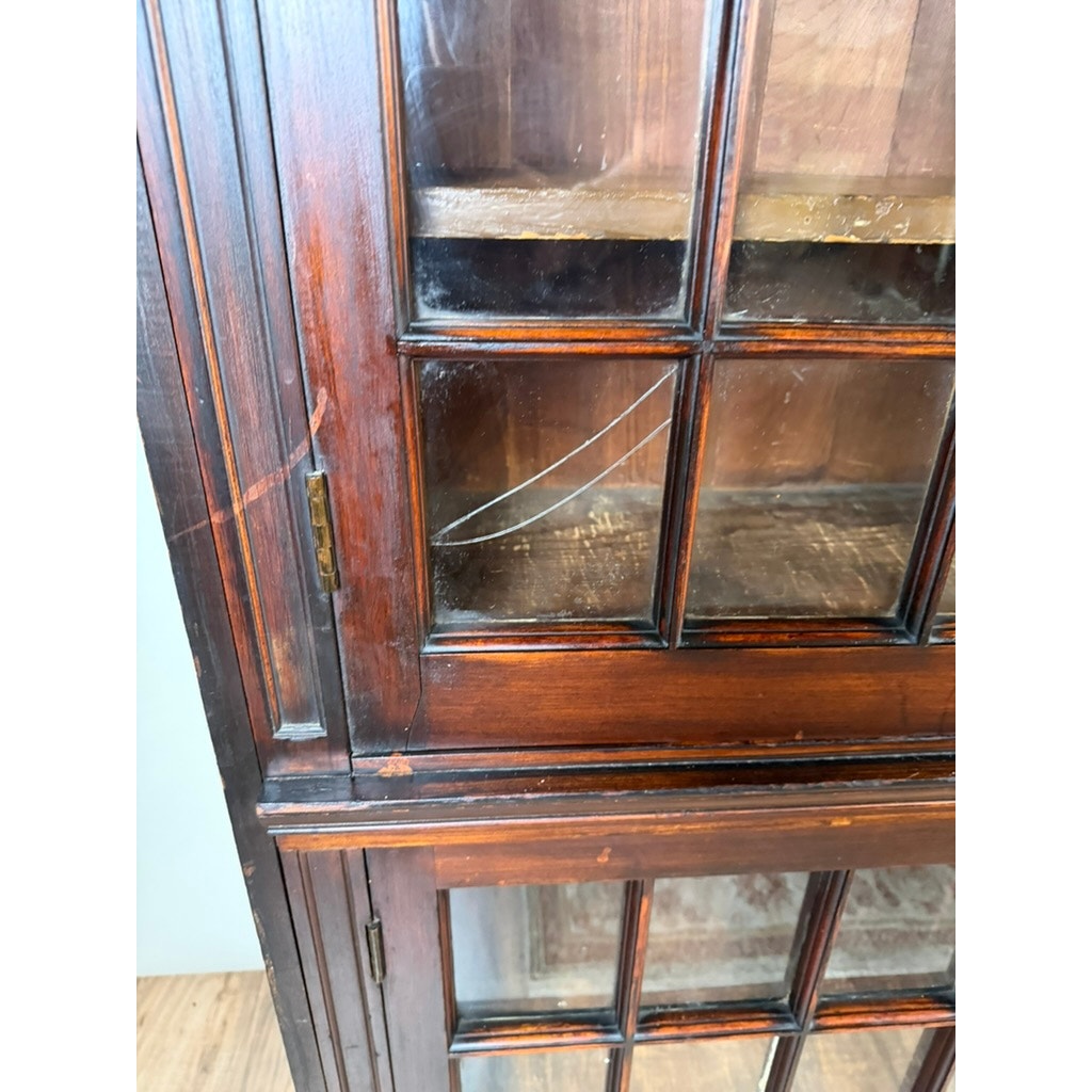 Close-up of one door from a Pair of Mid-19th Century New England Cherry Glazed Display Cupboards by Pearl City Antiques, c. 1840–1860; the dark, glossy cherry wood surrounds glass panes, with a prominent crack visible in one pane. The shelves and interior are clearly seen through the glass, evoking classic early American cupboard design.