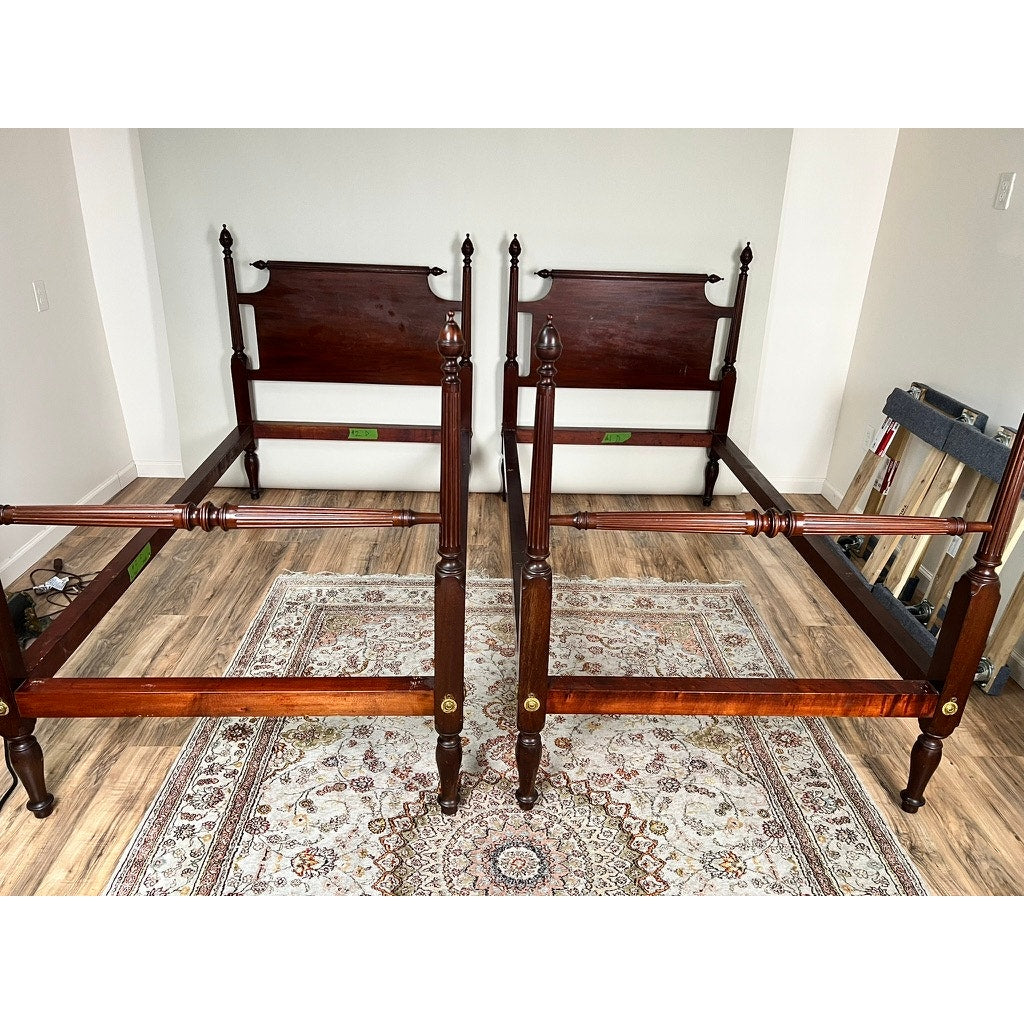A Vintage Pair of Centennial Solid Mahogany Twin Four Poster Beds c. 1940 stand side by side on a patterned area rug in a light-walled, wood-floored room, with tools and frames stacked against the right wall.
