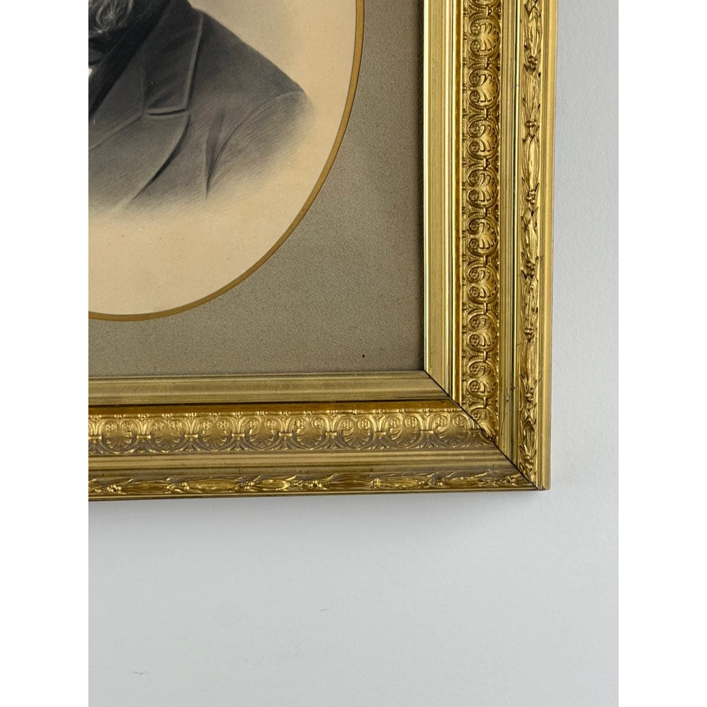 Close-up of the bottom right corner of an Antique Civil War Era Portrait of a Gentleman in Gilt Wood Frame, showing part of the sepia portrait and dark coat, set against a light-colored wall. Brand: Unknown.