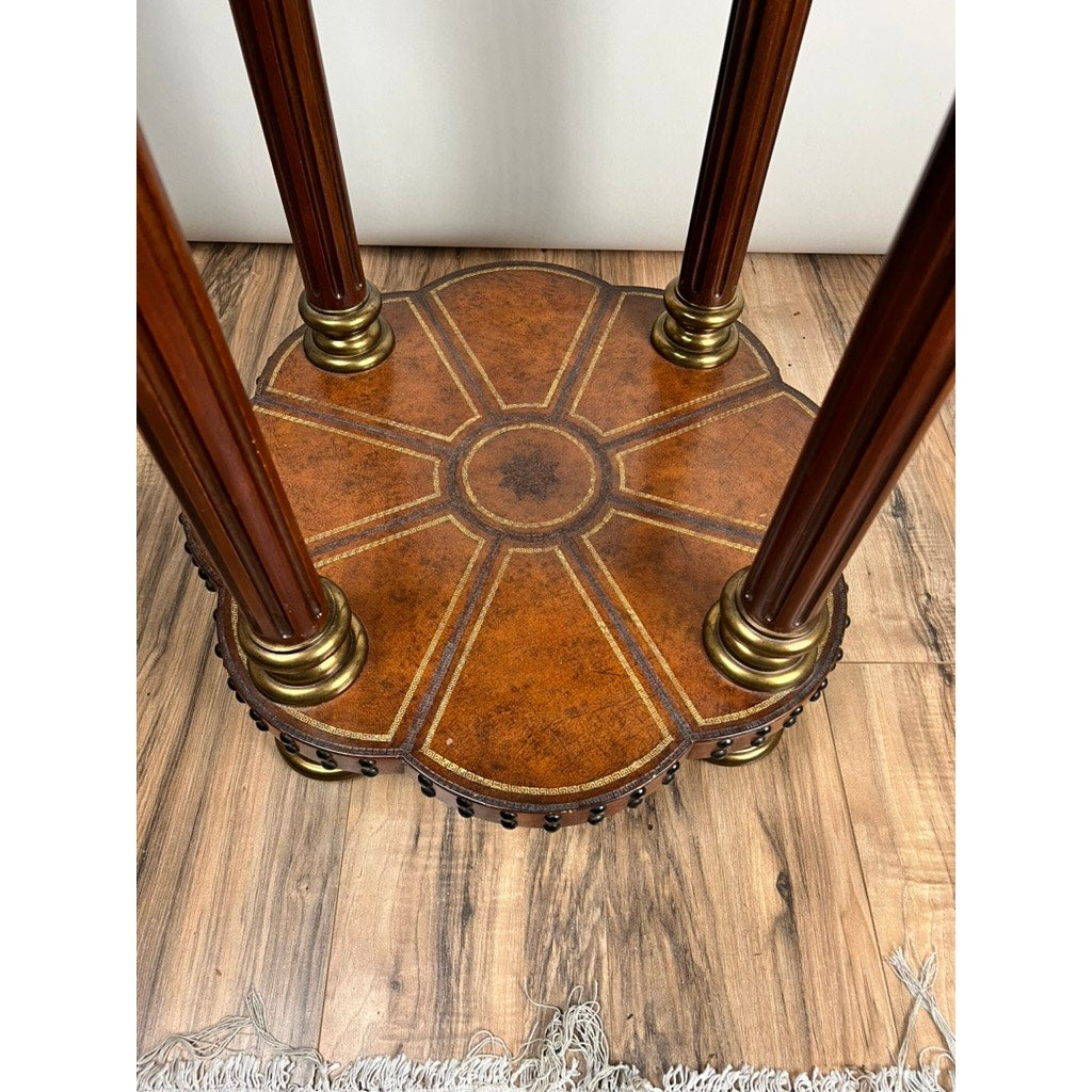 A close-up of the base of a Maitland Smith Vintage Maitland-Smith Leather-Clad Occasional Table shows four legs, a sunburst leather pattern, and brass accents complementing the wood floor; part of a rug appears at the edge.