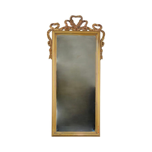 The Vintage Louis XVI Style Decorators Mirror is tall and rectangular, with a gold frame and an ornate ribbon-patterned crest at the top. The mirror has a plain white background, and its brand is unknown.