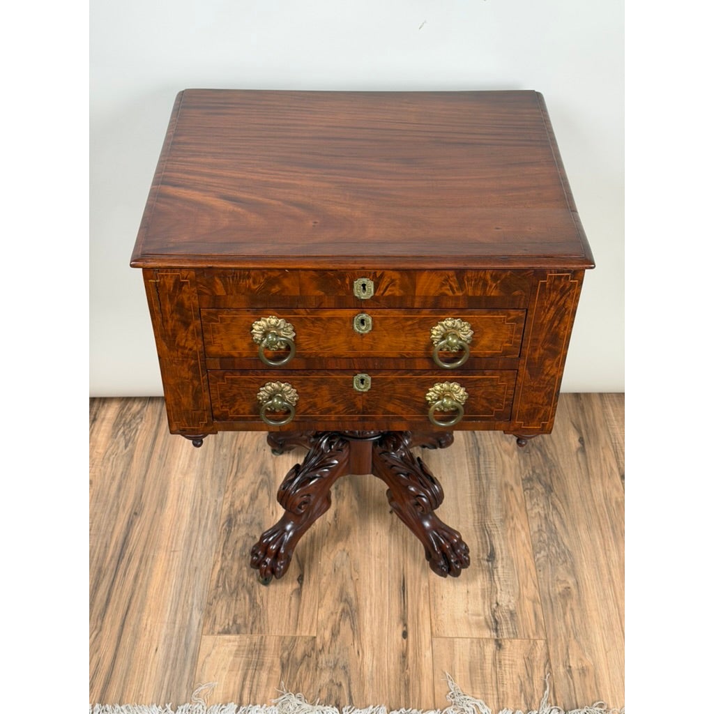 An American Classical Figured Mahogany Work Table, circa 1830–1845, featuring two drawers with brass ring pulls and a pedestal base with carved feet.