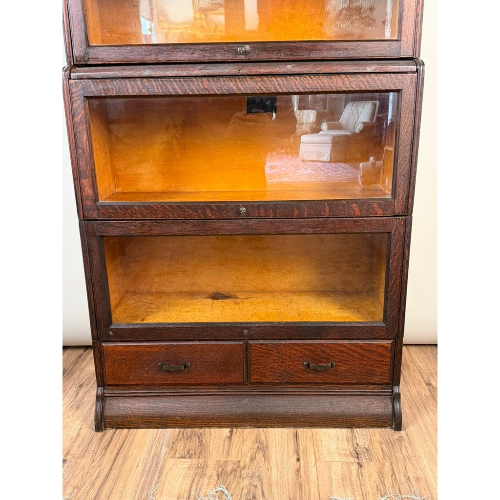 An Antique Hale System Quarter-Sawn Oak Five-Stack Barrister Bookcase by Camden Cabinet Company, c. 1910, with two glass-fronted shelves and two small drawers at the bottom, sits empty on a wood floor. The interior is unfilled, and a room reflection can be seen in the glass.