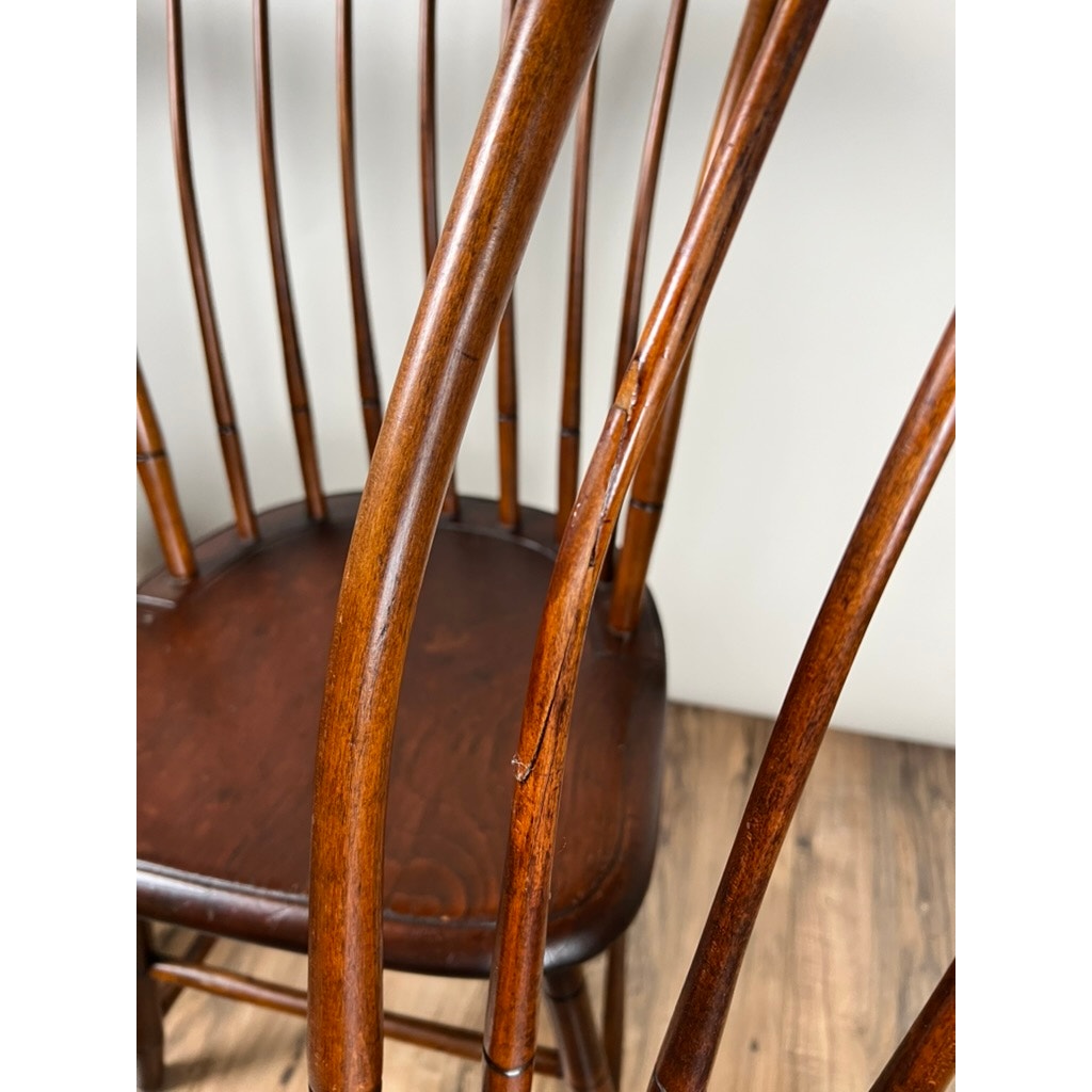 Close-up of a JR Hunt Antique NH Step Down Windsor Chair (set of 4, early 19th c.), showing its vertical back spindles—one with a visible crack. The dark wooden seat matches the similarly toned floor below.