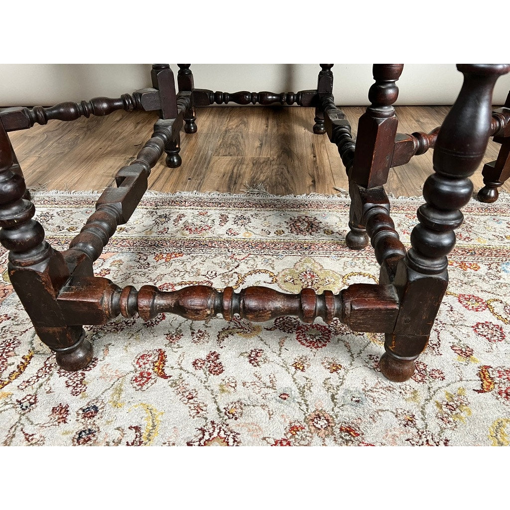Close-up of intricately carved legs and stretchers on an Antique English William & Mary Walnut One Drawer Gateleg Dining Table, c. Early 18th Century, shown atop a patterned red, yellow, and beige area rug over hardwood floors.