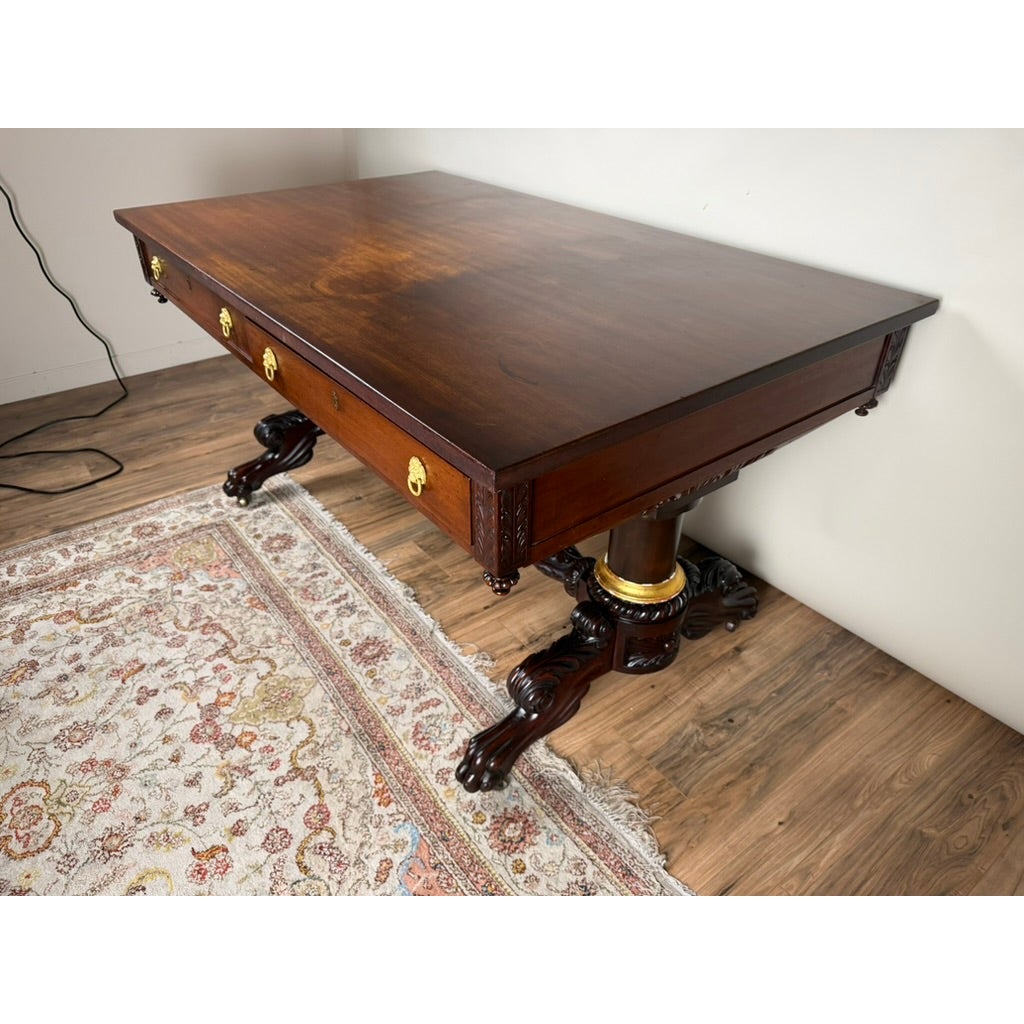 New York Classical Revival Carved Mahogany Double-Pedestal Library Table by Ernest F. Hagen, featuring three drawers with gold-toned lion head pulls and dual pedestals with carved feet and gold-finished collars.