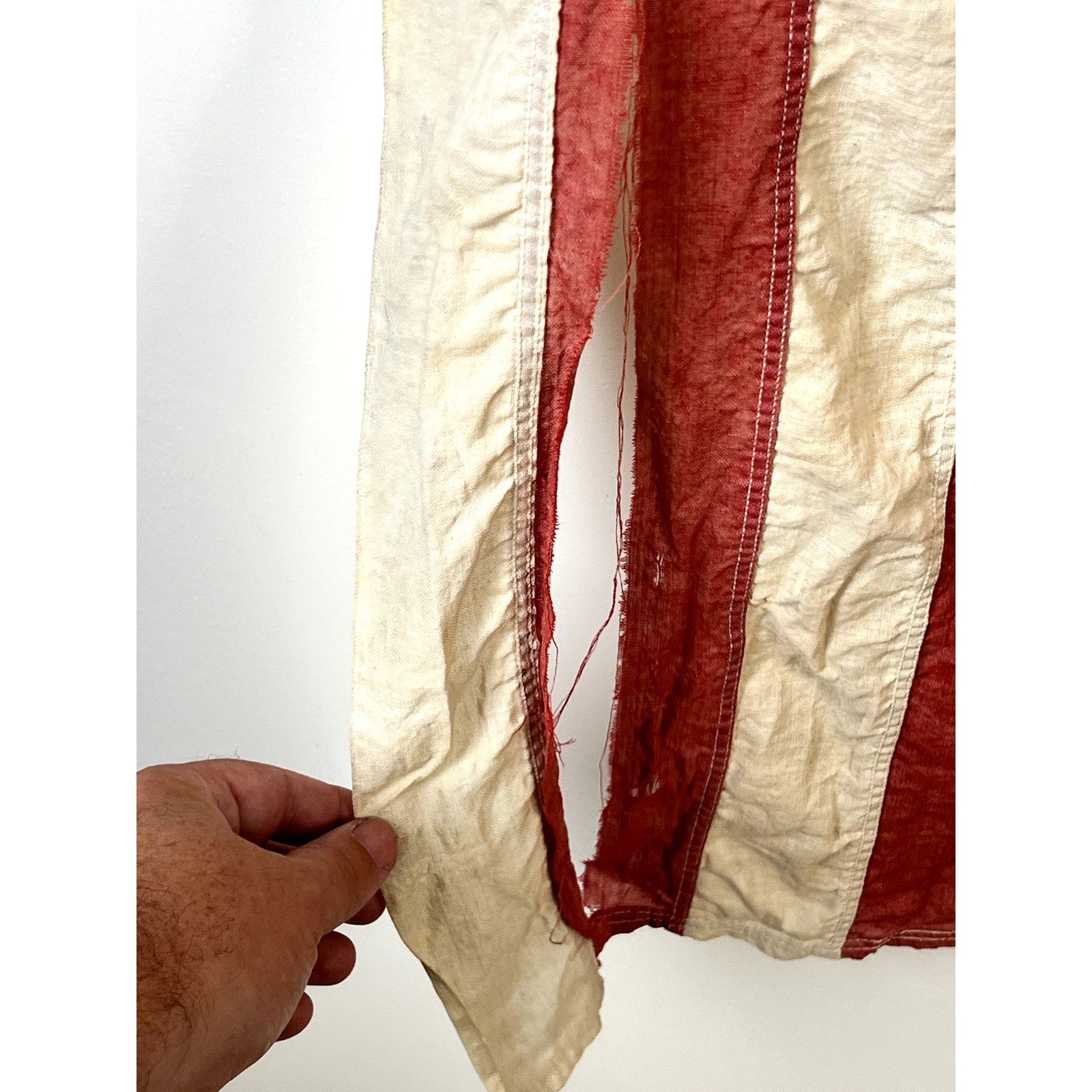 A hand holds the frayed edge of a Vintage Valley Forge “76” Bennington American Flag from the Bicentennial era (c. 1976), its aged red and white stripes set against a plain white background, evoking classic Americana nostalgia.