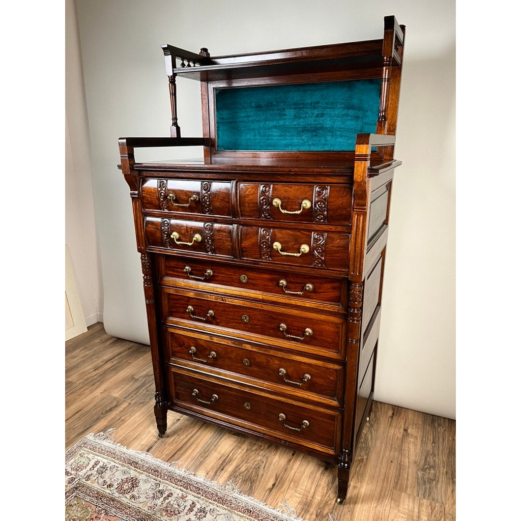 An Antique Victorian Aesthetic Movement Mahogany Four Over Four Gentlemen’s Chest c. 1880, featuring multiple drawers and a decorative top shelf with a teal fabric-lined back panel, stands on a wooden floor near a patterned rug.