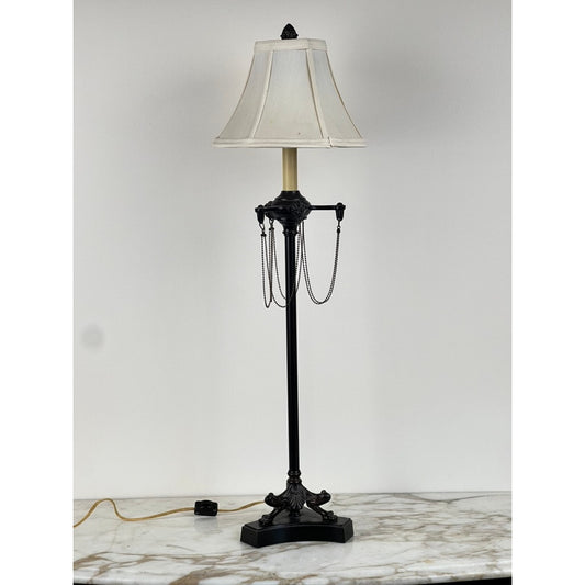 Pearl City Antiques’ Vintage French Empire Revival Table Lamp in an oiled bronze finish features an ornate base, a white lampshade, and classic pull chains, elegantly displayed on a marble surface against a plain white wall.