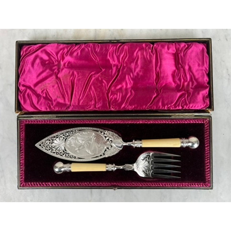 The Antique Victorian Silver-Plated Fish Serving Set includes a serving knife and fork with ivory-colored handles, housed in its original presentation box lined with magenta and burgundy satin fabric.