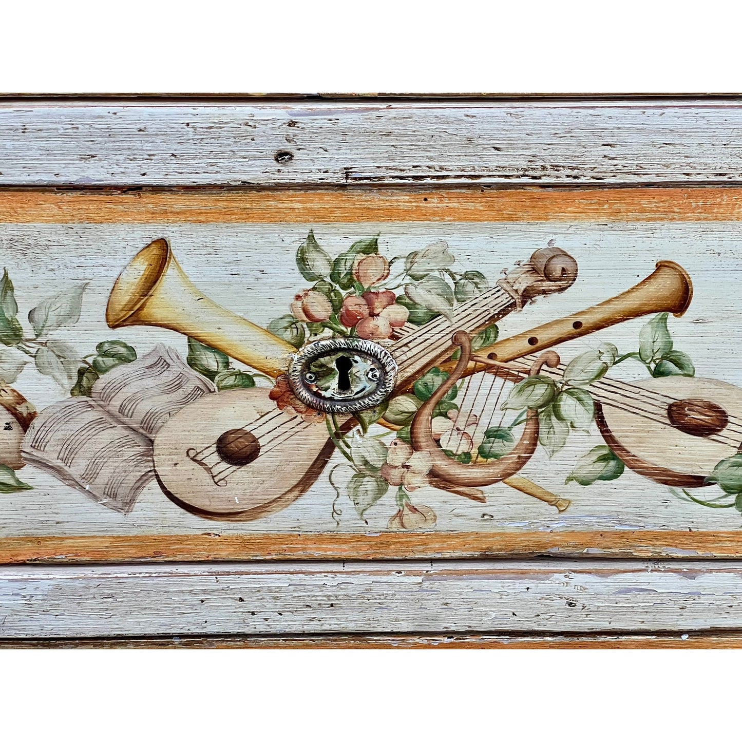 The Antique Italian Paint Decorated Four Drawer Commode c. Early 19th Century features a painted design of a trumpet, lute, lyre, sheet music, pink flowers, and green leaves on weathered wood surrounding an ornate keyhole.