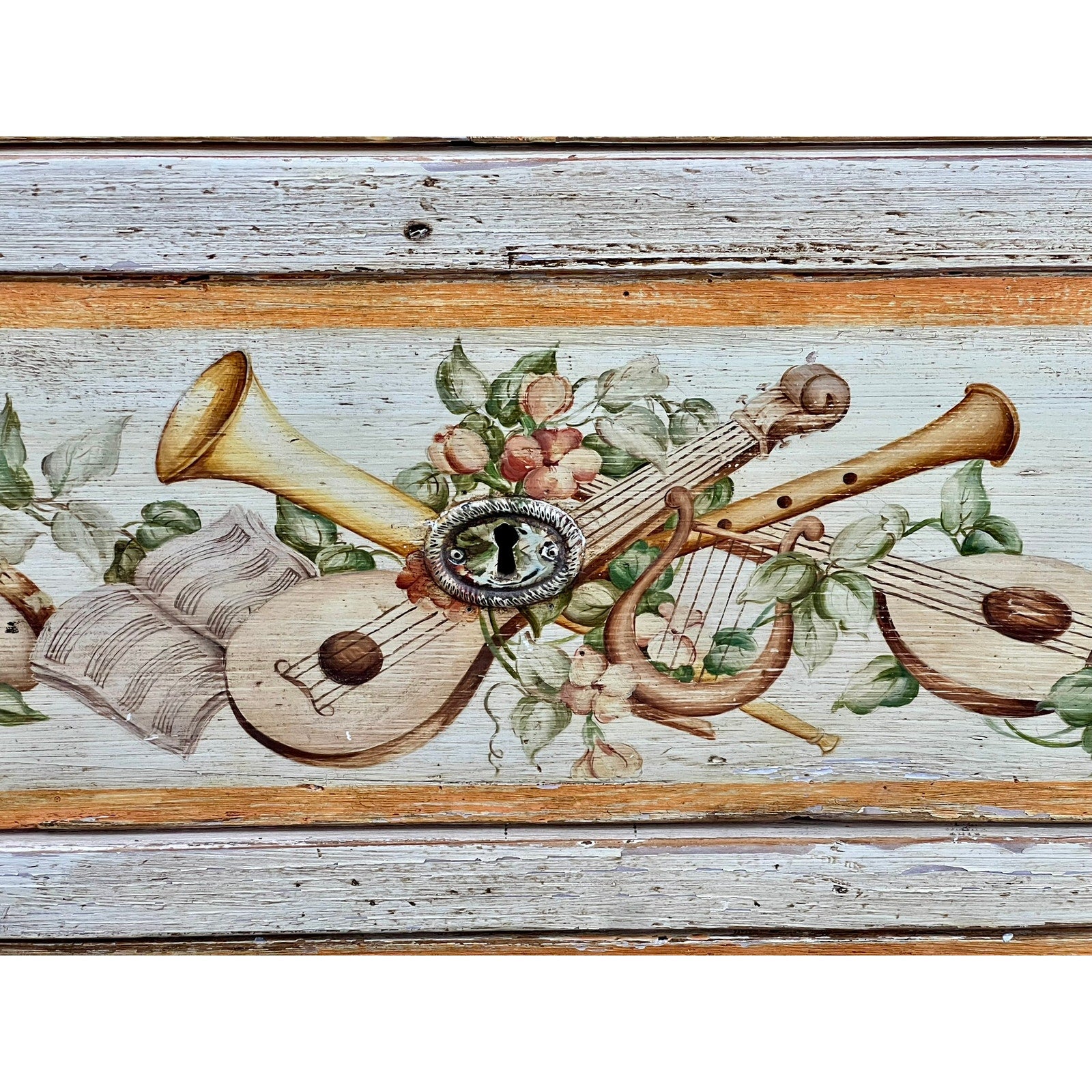 The Antique Italian Paint Decorated Four Drawer Commode c. Early 19th Century features a painted design of a trumpet, lute, lyre, sheet music, pink flowers, and green leaves on weathered wood surrounding an ornate keyhole.
