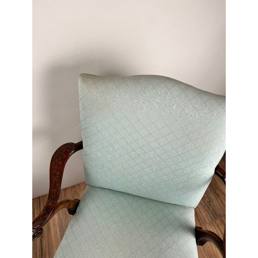 An Antique George II Mahogany Gainsborough Open Arm Chair (mid 19th century) with light blue diamond-pattern upholstery, carved wooden armrests, and a high back is set on a wood floor against a plain light wall.