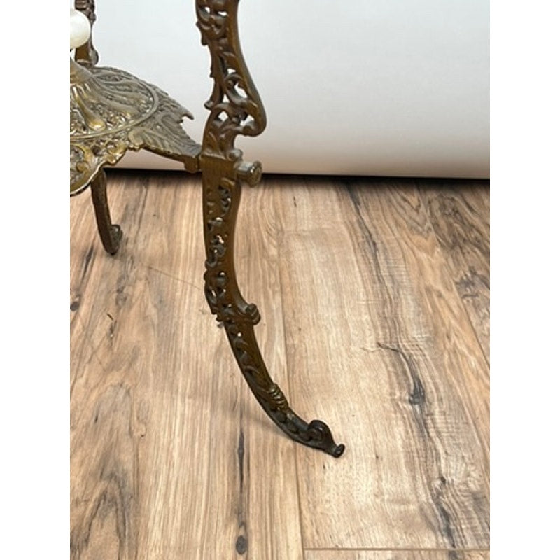 The ornate, curved metal leg of an Antique Victorian Bronze and Onyx Stand (late 19th century) with intricate detailing stands on a light brown wood floor with visible grain, set against a white background. Brand: Unknown.
