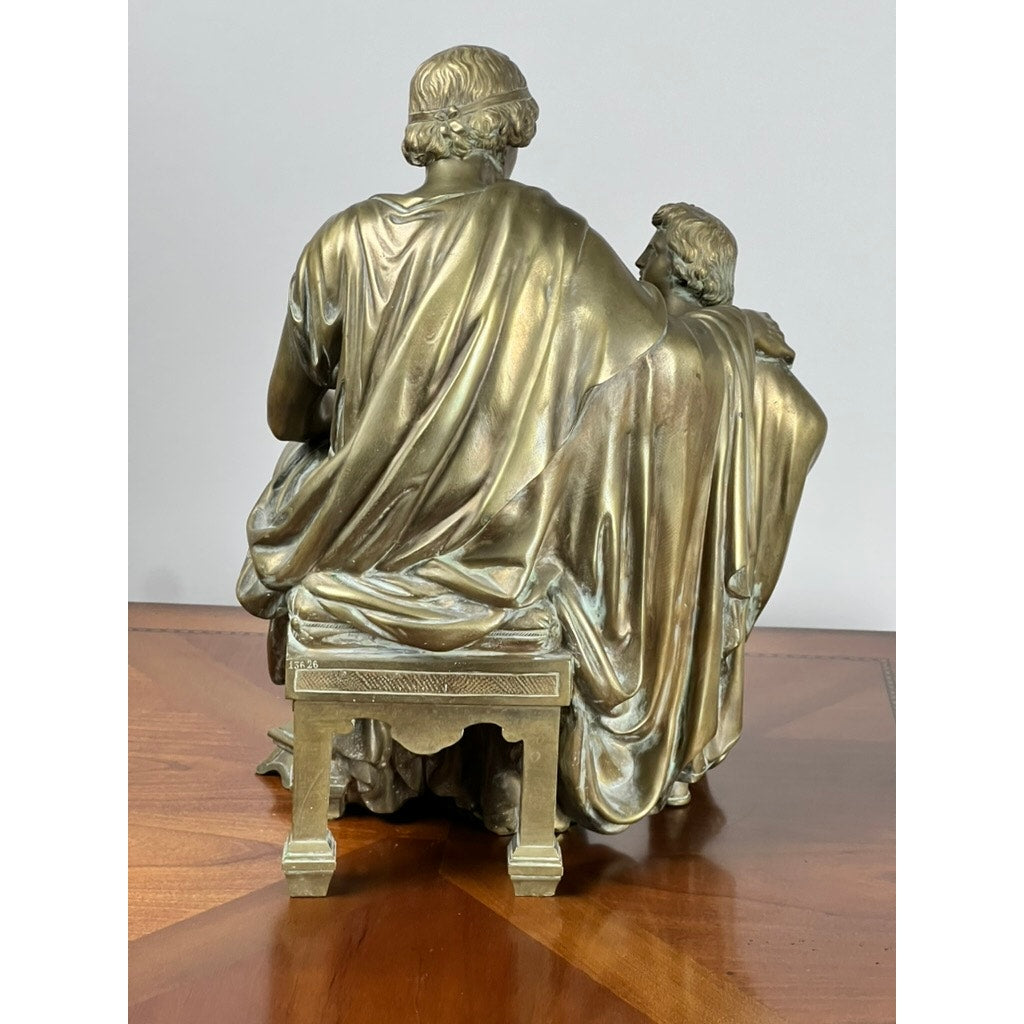The “Teacher and Pupil” Antique Bronze Sculpture by Louis Charles Janson (1865, signed Ch. Janson) shows two figures in robes seated on a detailed bench, viewed from behind and displayed on a wooden surface.