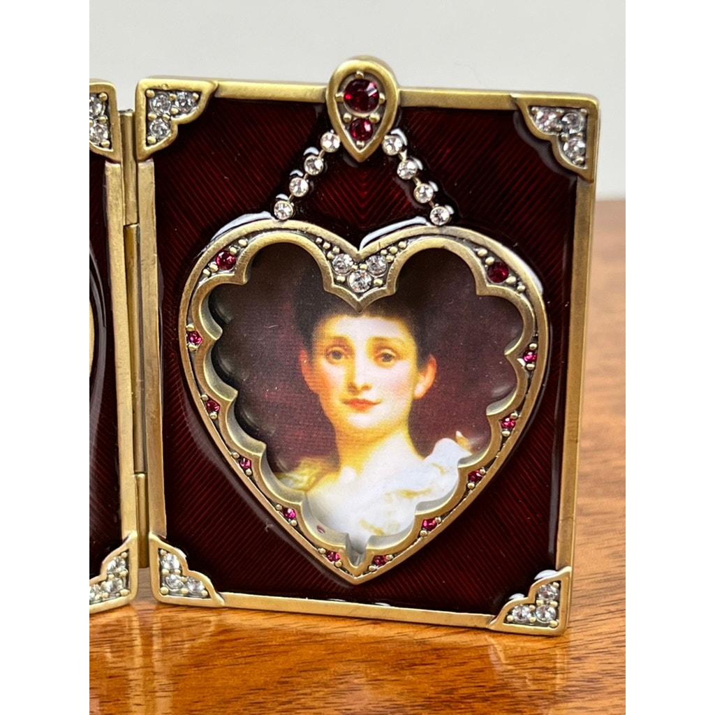 The Jay Strongwater Bejeweled Enamel Double Heart Picture Frame features delicate jeweled accents, beautifully showcasing a painted portrait of a young woman in white against a red and gold decorative backdrop.