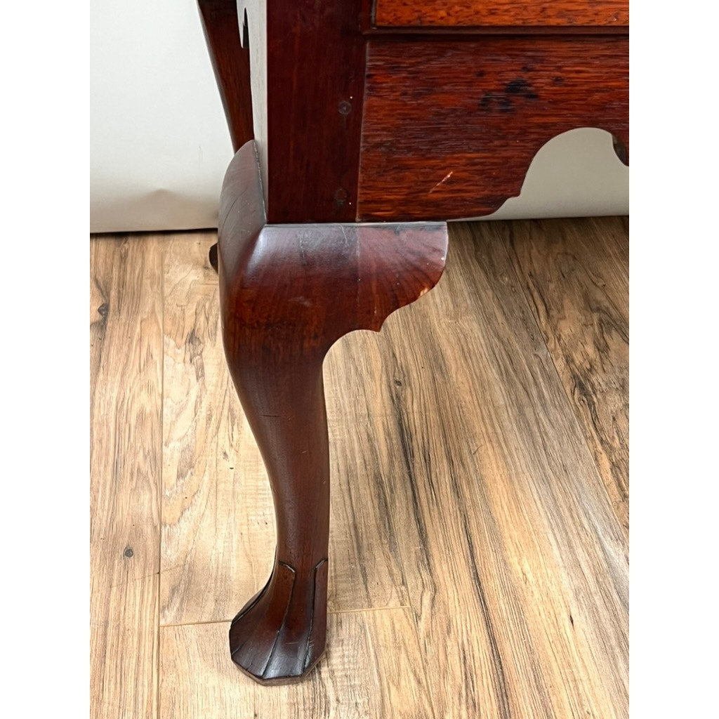 Close-up of a carved drake foot in dark walnut from an Antique Queen Anne Chest on Frame, probably Irish, late 18th century. The claw-like, curved leg stands on a light wooden floor, showcasing classic craftsmanship. Brand unknown.
