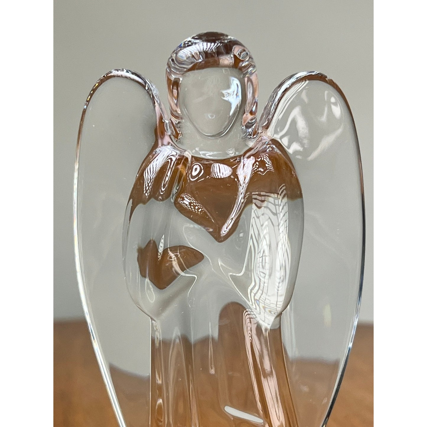 The Vintage Baccarat Crystal Angel by Baccarat is a clear crystal figurine with folded arms and etched details, displayed on a wooden surface against a plain background.