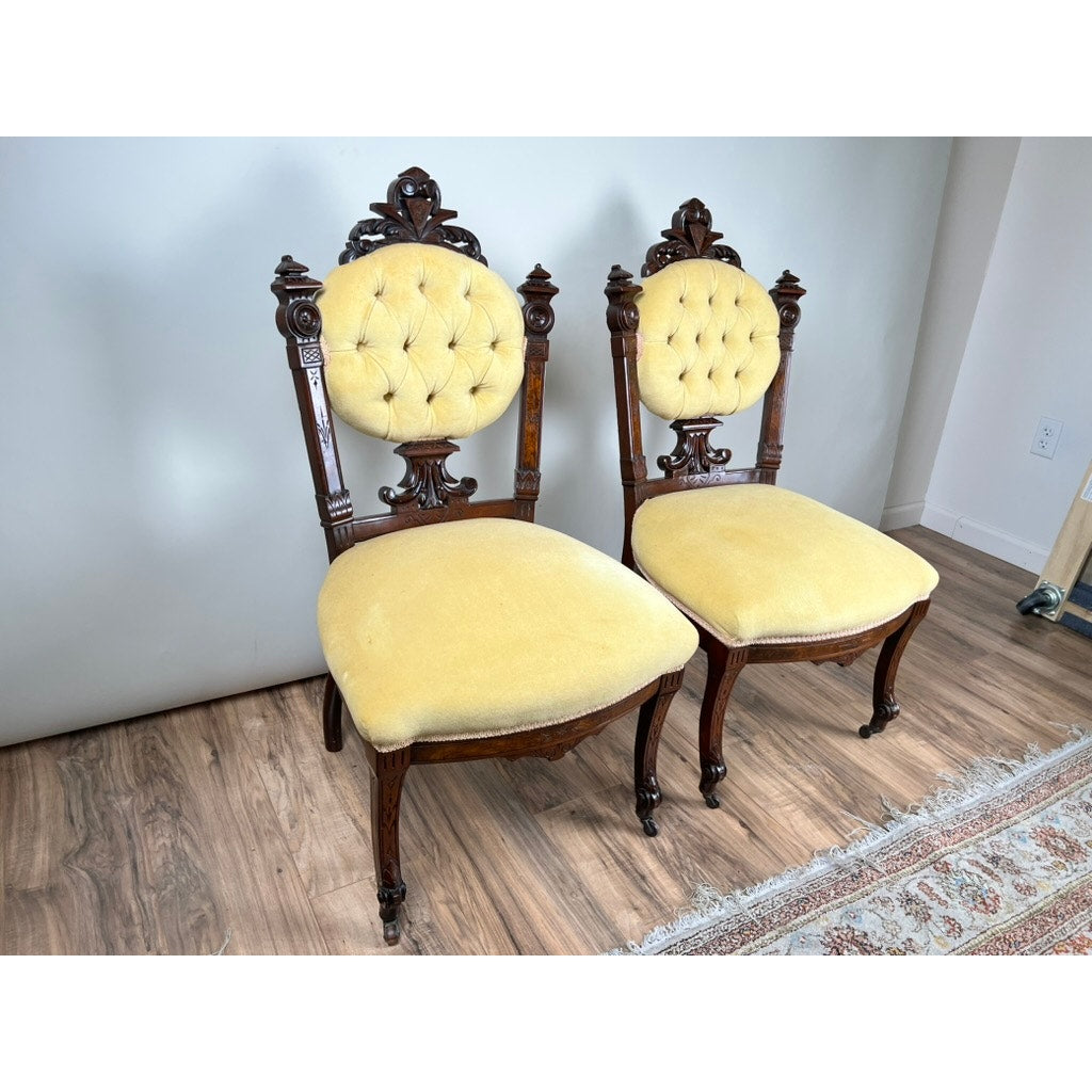 Fine Antique Pair Renaissance Revival Walnut Side Chairs, attributed to John Jelliff, Newark c. 1880, featuring ornate carved backs and legs with yellow upholstered seats and button-tufted round backs, displayed on wood flooring beside a patterned rug.