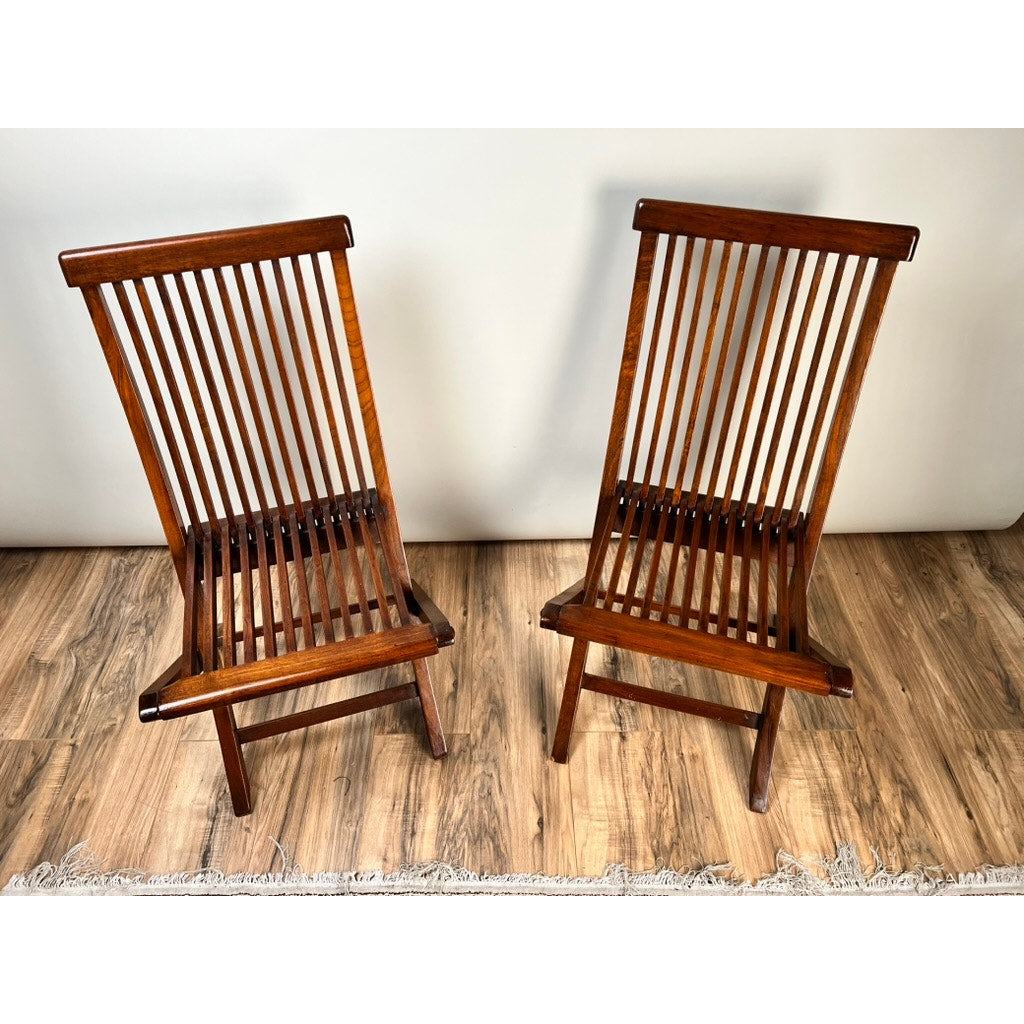 A Pair of Vintage Mid-Century Modern Style Teak Folding Chairs are placed facing each other on a wooden floor, against a light wall with part of a fringed rug visible. Brand: Unknown.